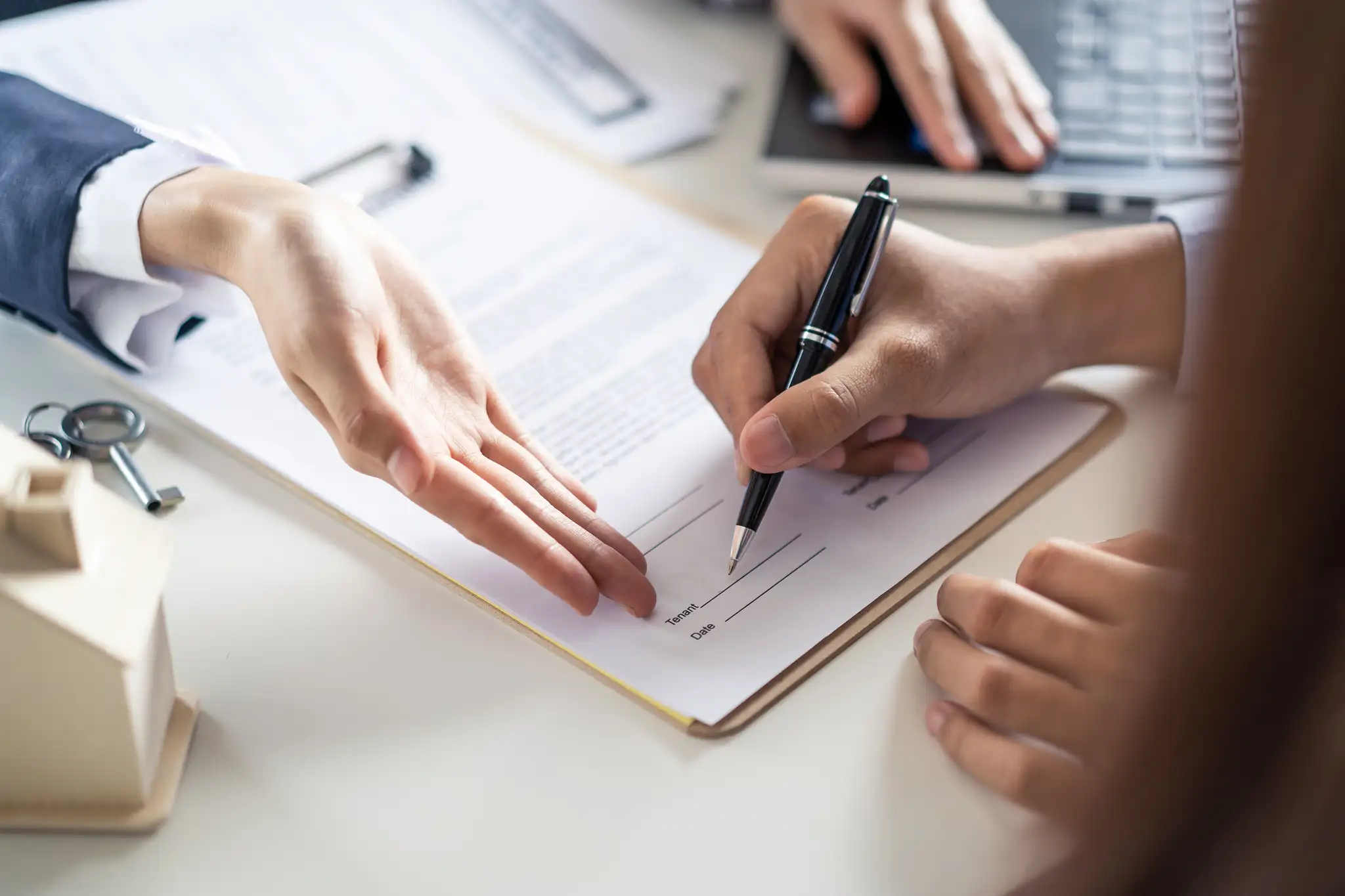 Podpisywanie umowy sprzedaży domu przez klientów, z kluczykami i dokumentami na biurku.