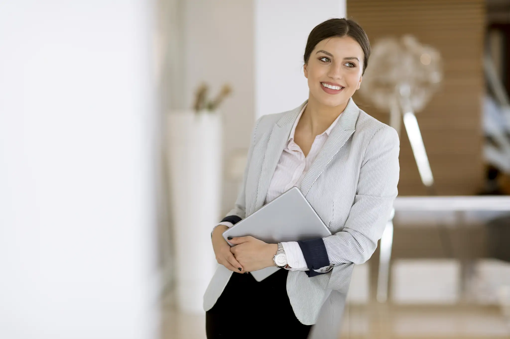 Uśmiechnięta agentka nieruchomości z tabletem w eleganckim biurze, gotowa do obsługi klienta.